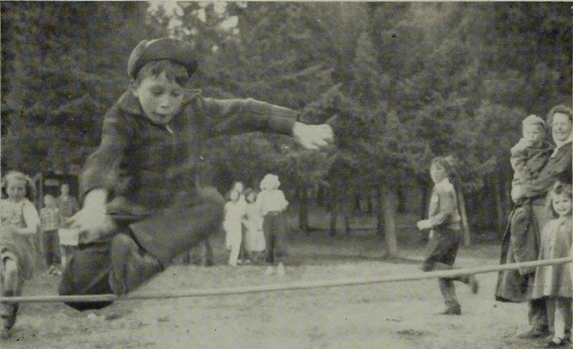 A black and white photograph of a young boy jumping over a bar.